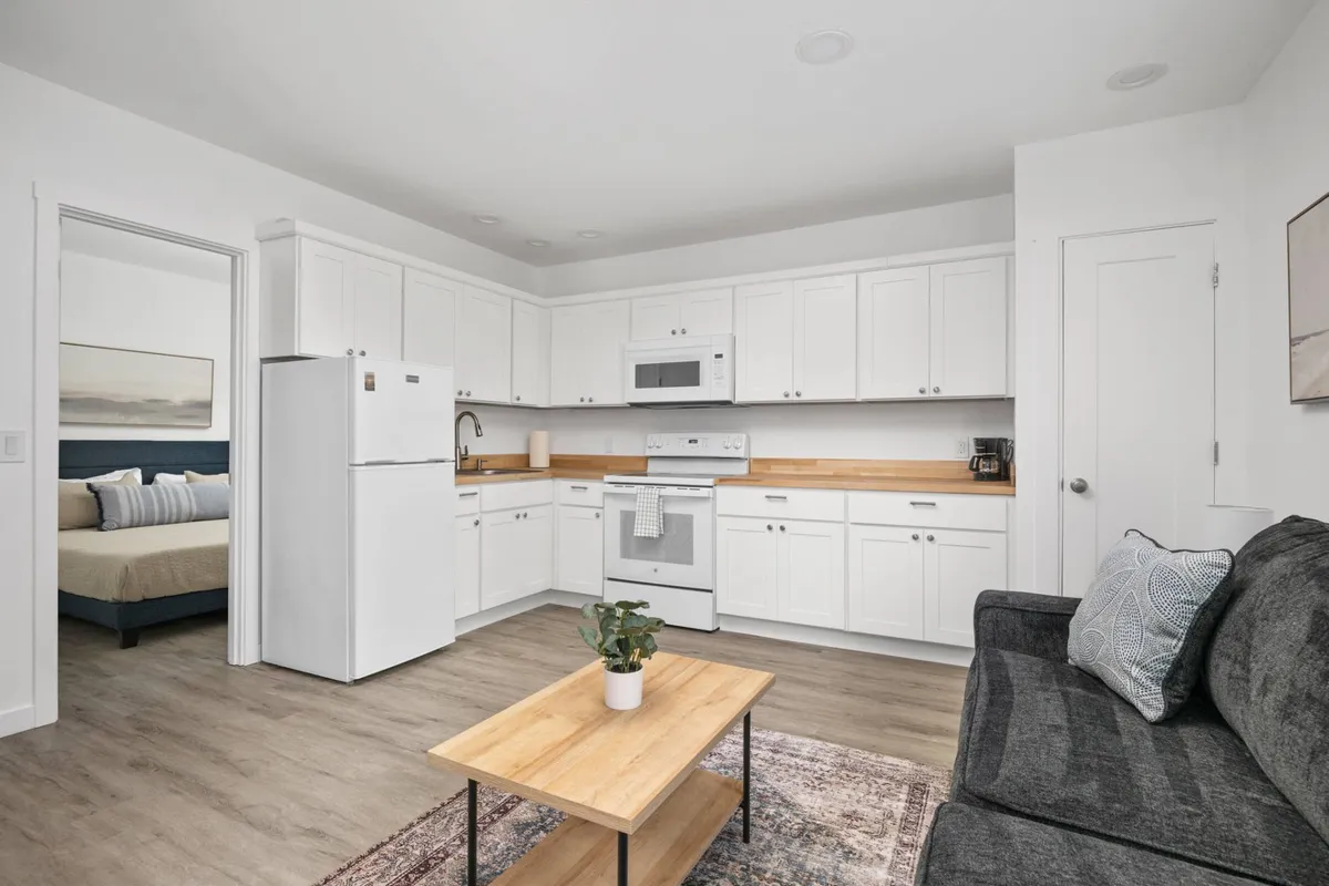 An inviting open-plan living and kitchen area featuring a comfortable sofa, kitchen counter, and coffee table. The space is bright, airy, and tastefully decorated with modern furnishings, capturing the room's versatility for both relaxation and entertaining.