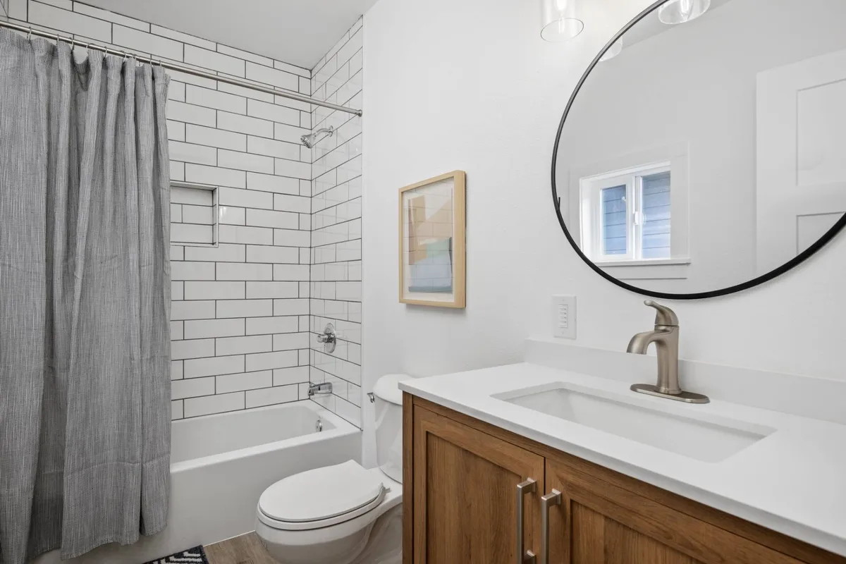 A modern bathroom with a round mirror, wooden vanity, framed artwork, and a subway tile wall. The atmosphere is calm and refreshing, providing a relaxing space to unwind and prepare for the day.