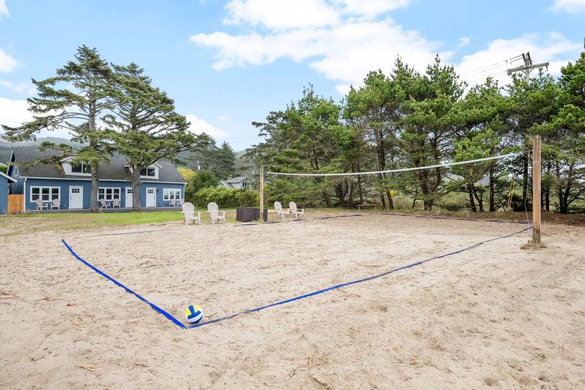 This exterior image captures a lively scene with a volleyball court set against a backdrop of beach chairs, surrounding trees, and a clear blue sky. The court is ready for play, while the nearby chairs and lush landscape suggest a relaxed, communal atmosphere perfect for both activity and leisure.