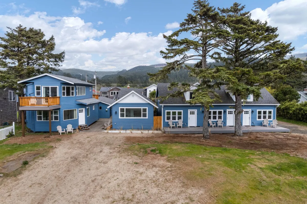 This image shows the blue house exterior under large trees, with a comfortable outdoor seating area. The porch offers a peaceful place to relax, and the presence of trees suggests plenty of shade for pets and owners alike after time spent at the beach.